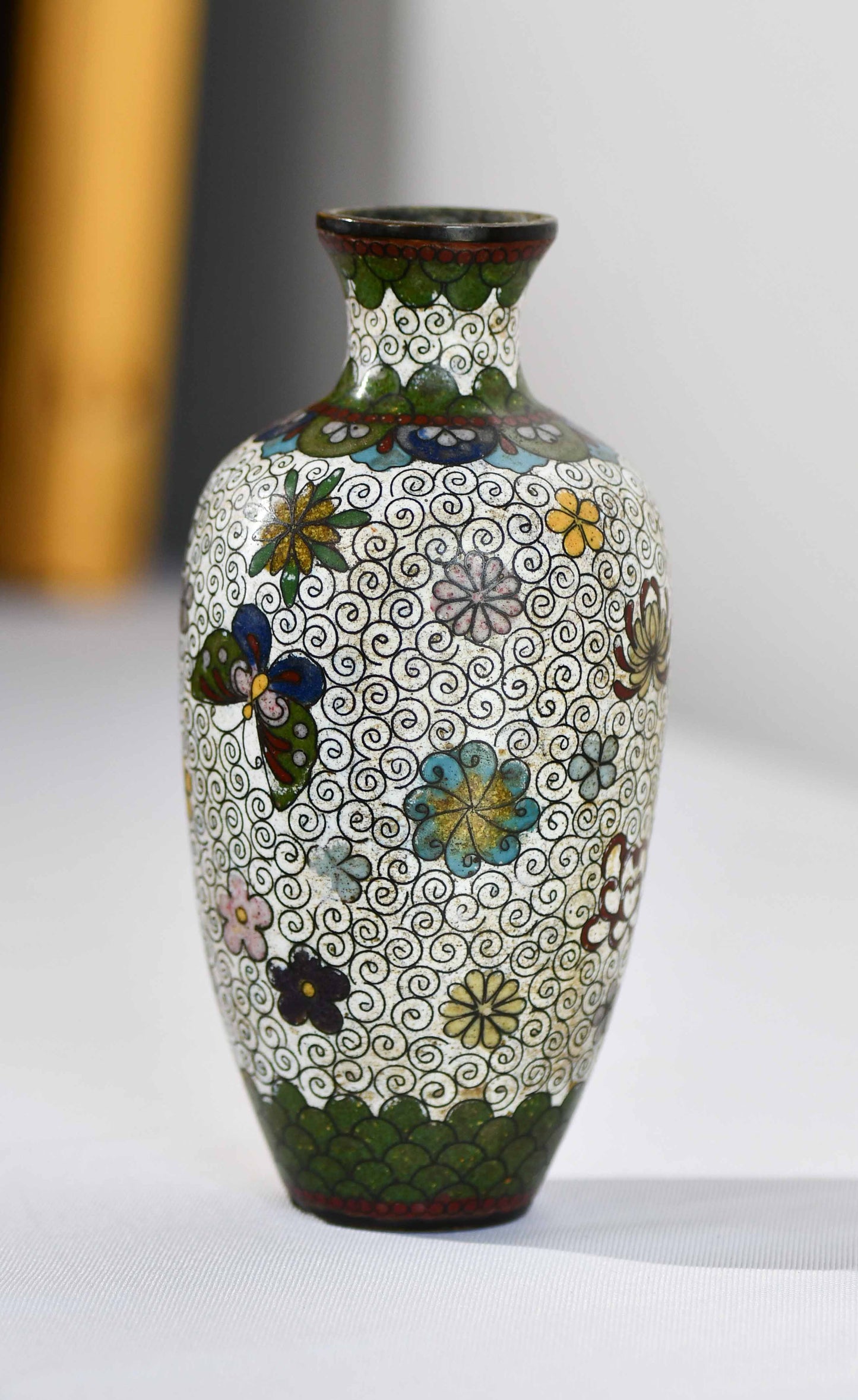 A Japanese Meiji style cloisonne vase with white floral pattern and butterflies against a dense scrolled background.
