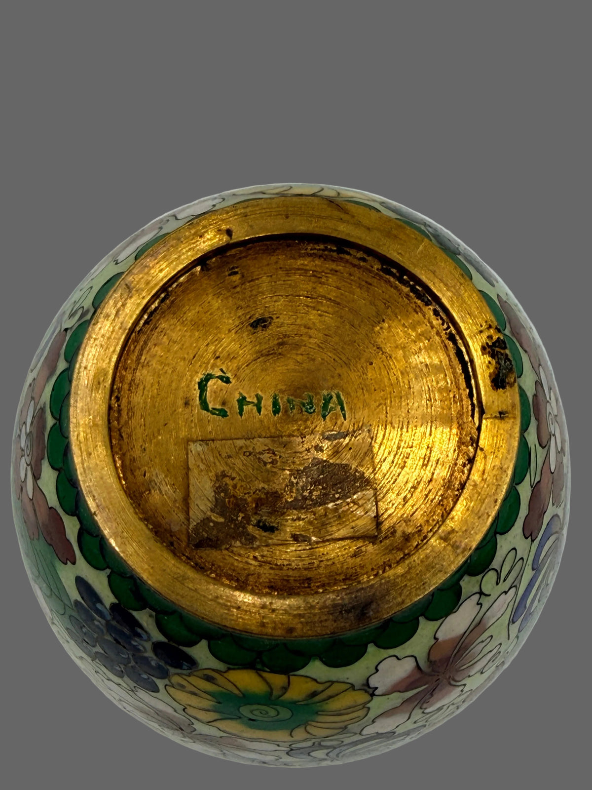 The bottom view of a Chinese porcelain vase or urn, showing a wide gold-colored glazed base with the word 'CHINA' hand-painted in green, surrounded by a floral pattern on the body.