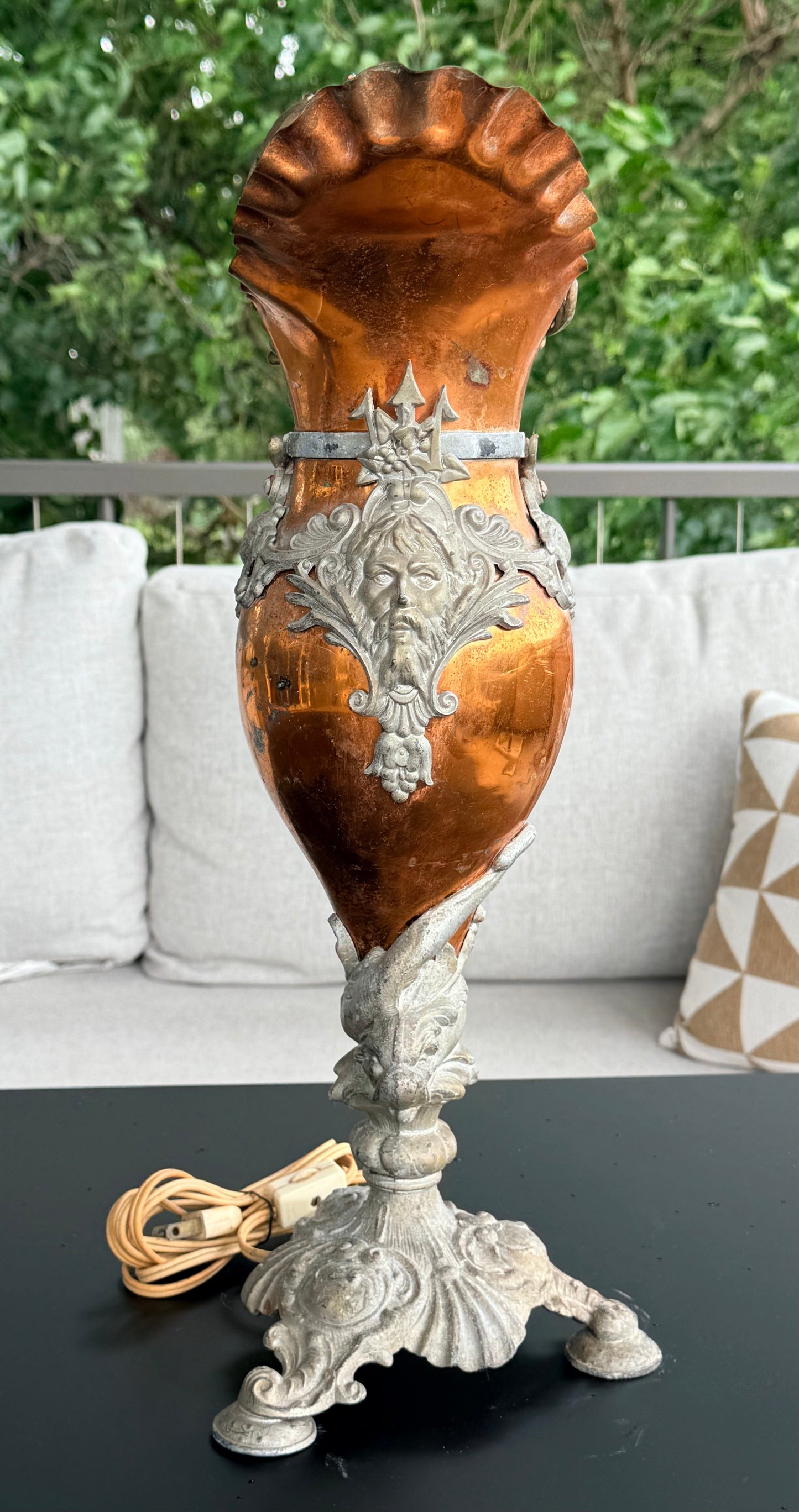 Decorative metal and wood vase on a black surface with a blurred outdoor background