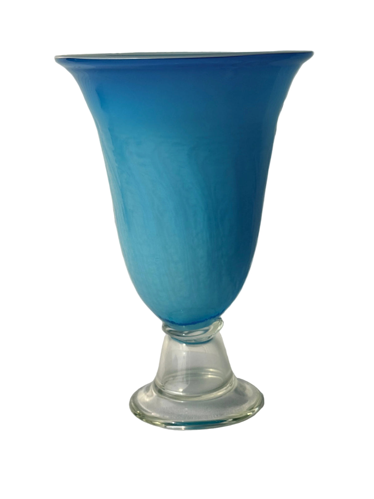 A vintage blue glass vase with a flared rim and a clear glass pedestal base, set against a white paneled wall.