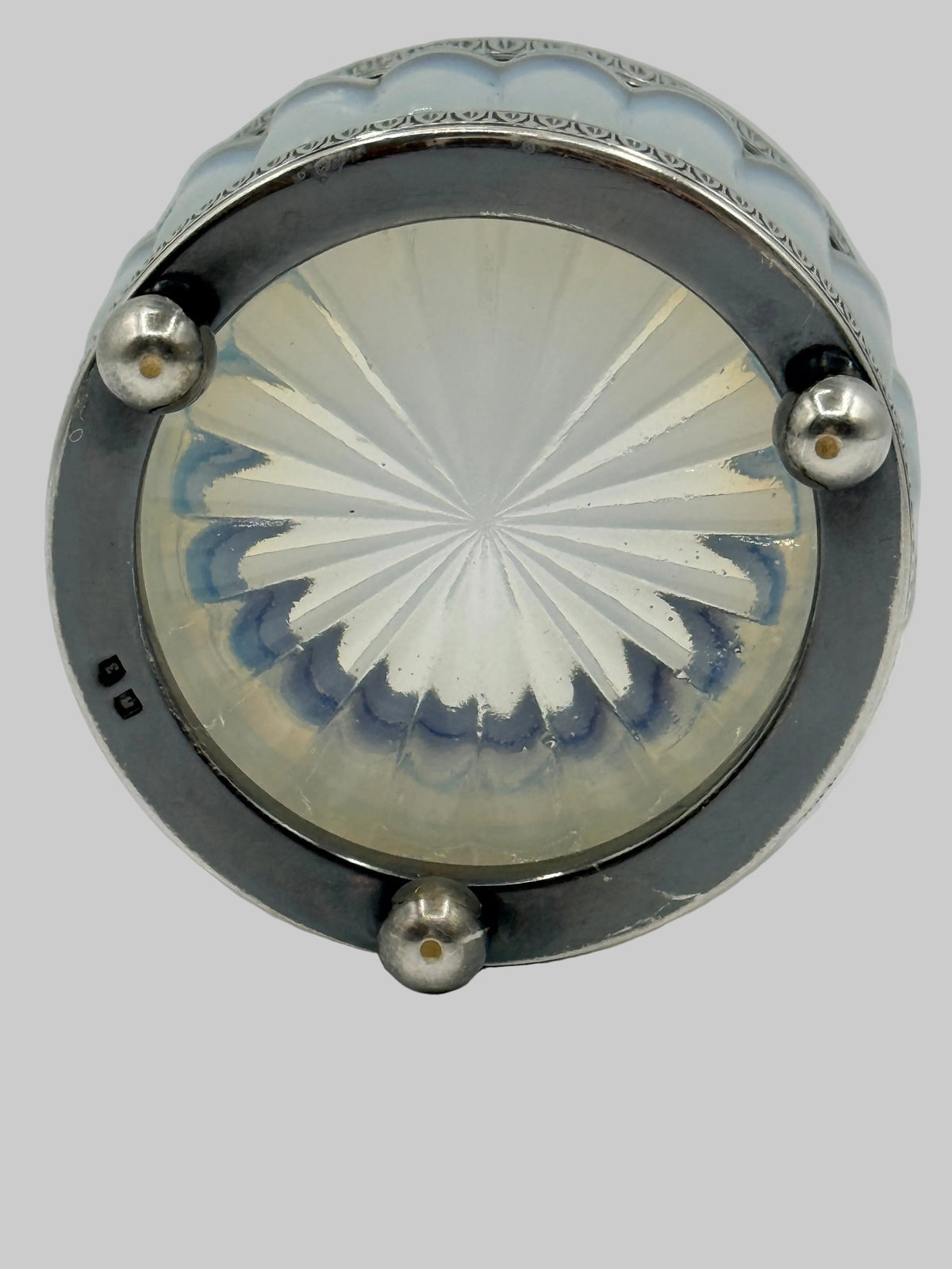 An antique circular glass and metal object, likely a decorative box lid or casket, featuring a silver-toned metal frame with three prominent silver rivets and a faceted, starburst-patterned glass insert.