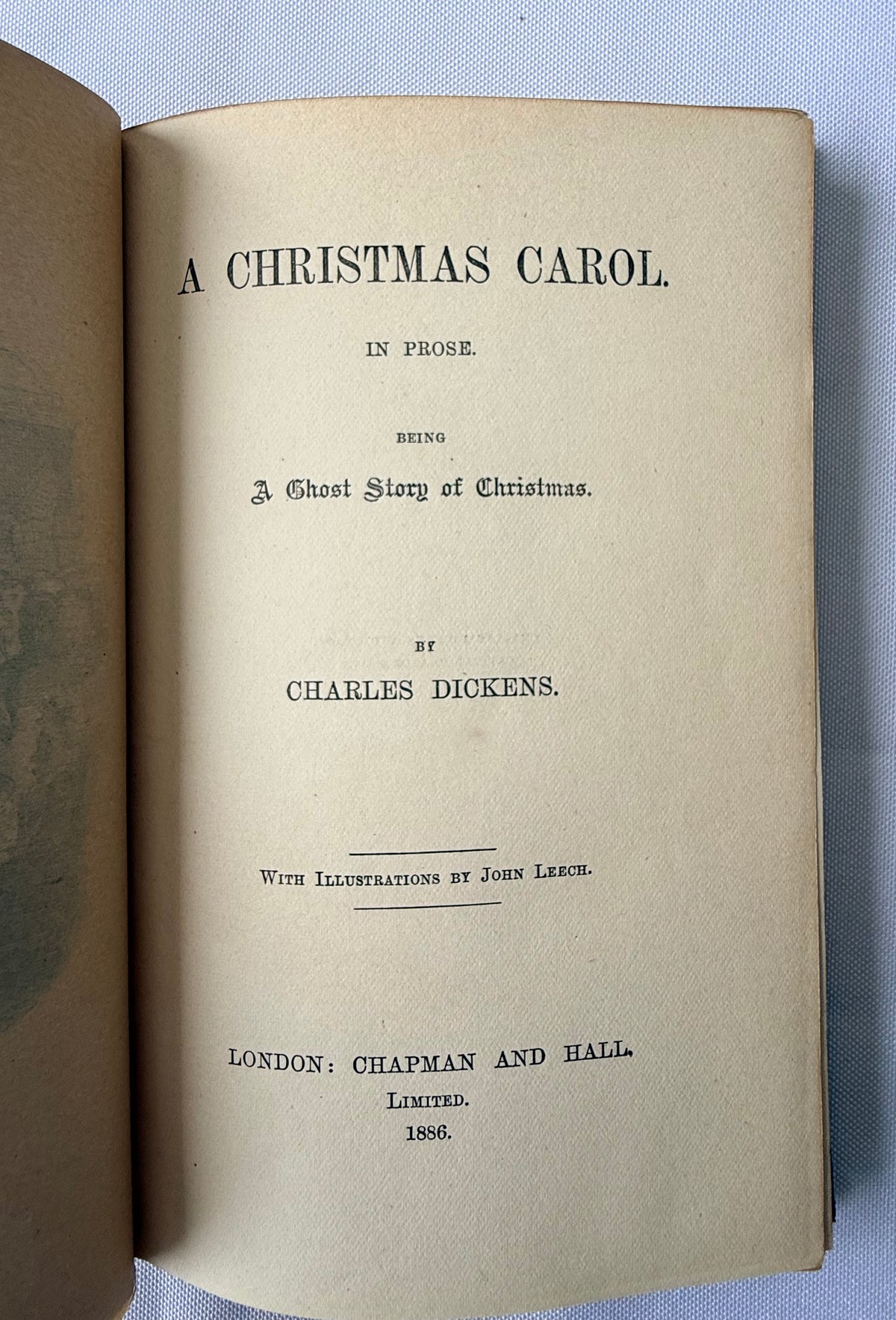 An open vintage book showing the title page of 'A Christmas Carol' by Charles Dickens, printed in black on aged beige paper, photographed against a light blue fabric background.