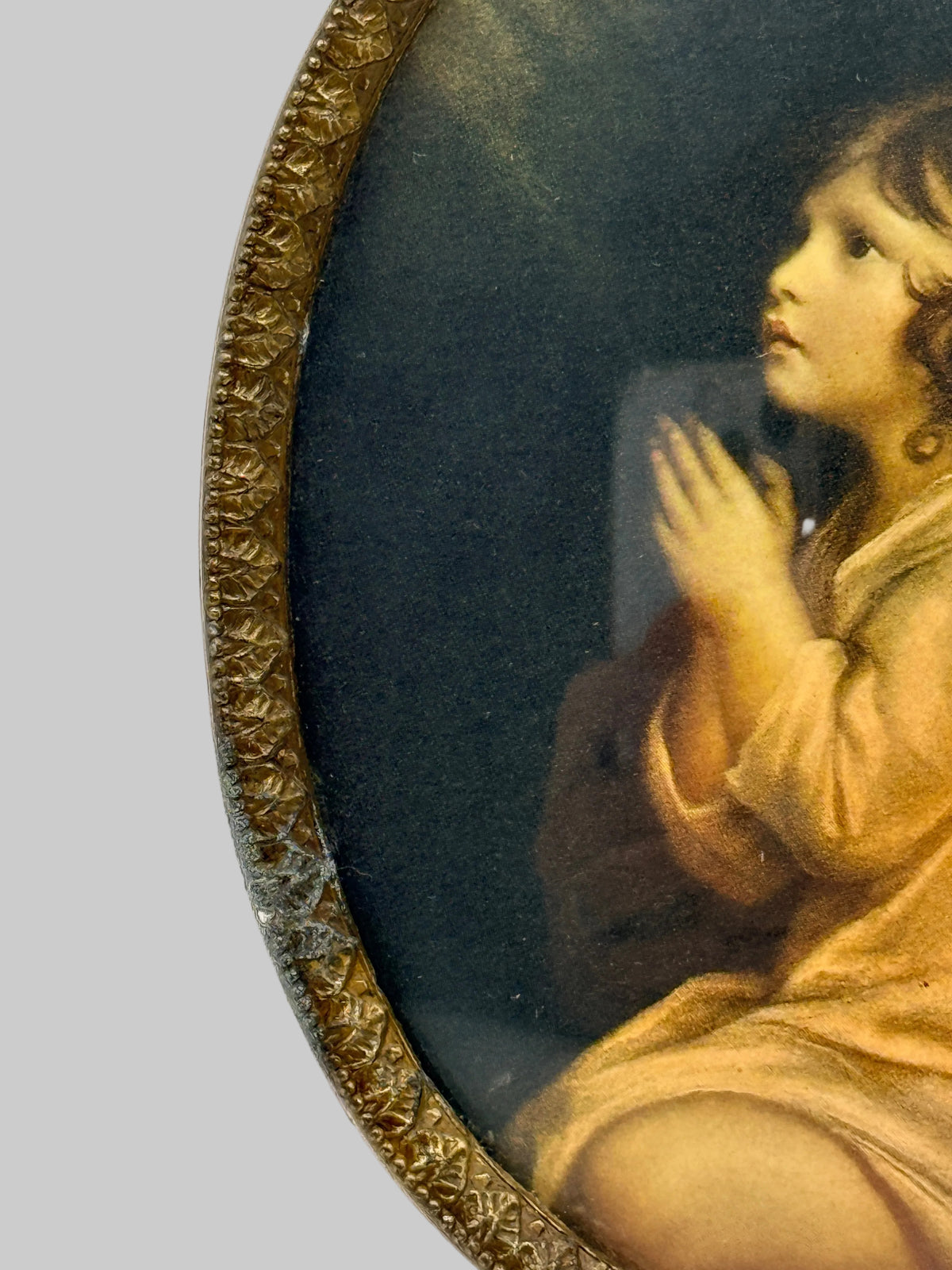 Close-up of an oval framed portrait painting showing part of a child in warm beige clothing against a dark background, with an ornate gold-toned frame visible on the left.