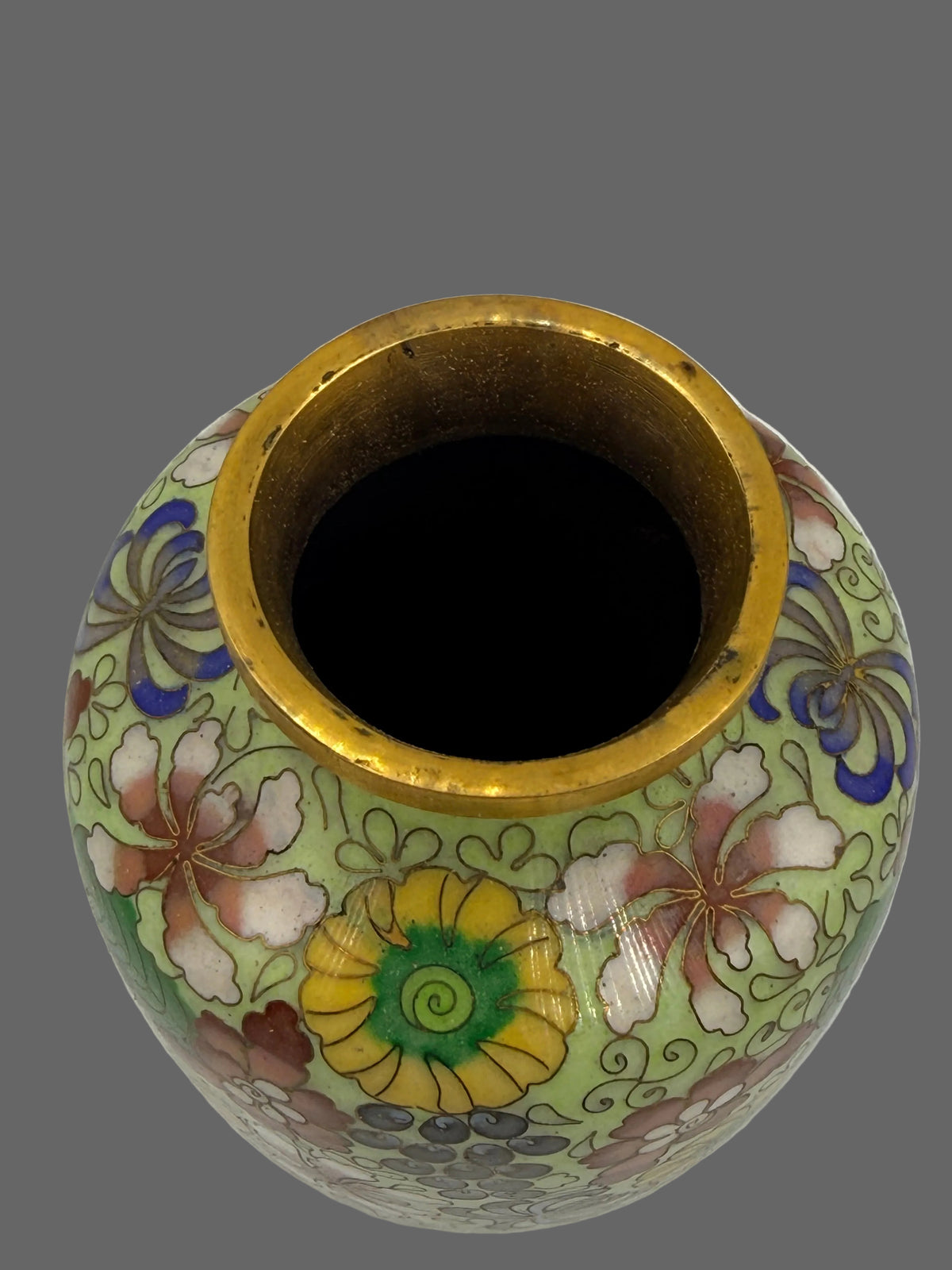 A round ceramic vase with a light green background, decorated with colorful floral motifs in pink, yellow, blue, and white, featuring a prominent gold-toned rim.