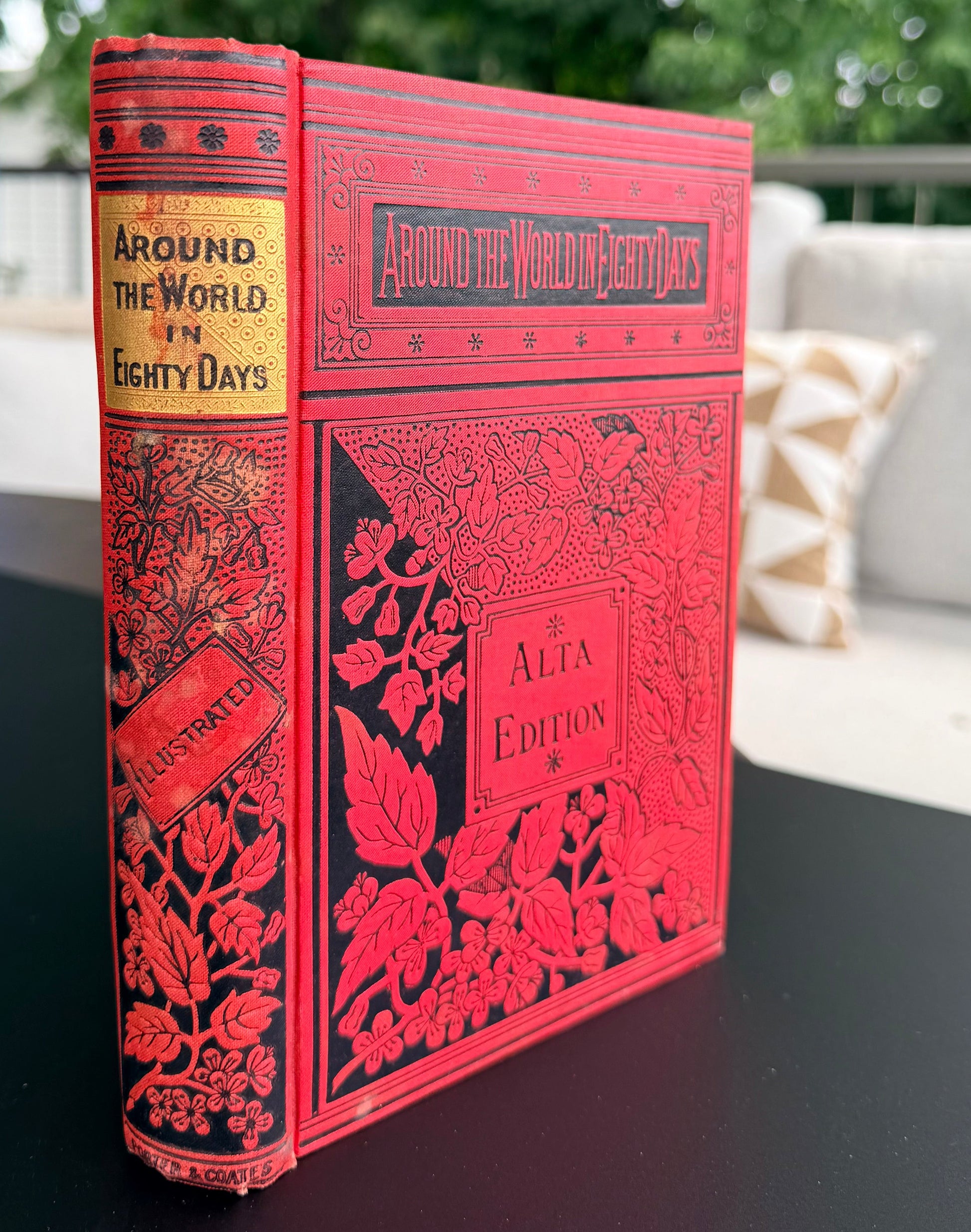 Red book titled 'Around the World in Eighty Days' on a black surface with a blurred outdoor background