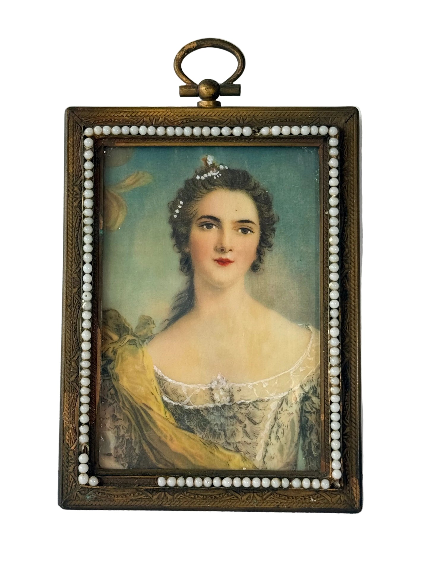 A framed vintage portrait print of a woman in an 18th-century style, featuring a dark ornate frame decorated with white faux pearls and a brass hanging loop at the top, set against a white paneled wall.
