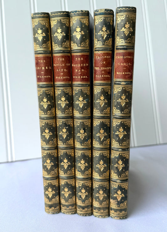 A set of five antique hardcover books standing upright, featuring dark green leather spines with ornate gold foil detailing and red cloth bands with gold lettering.