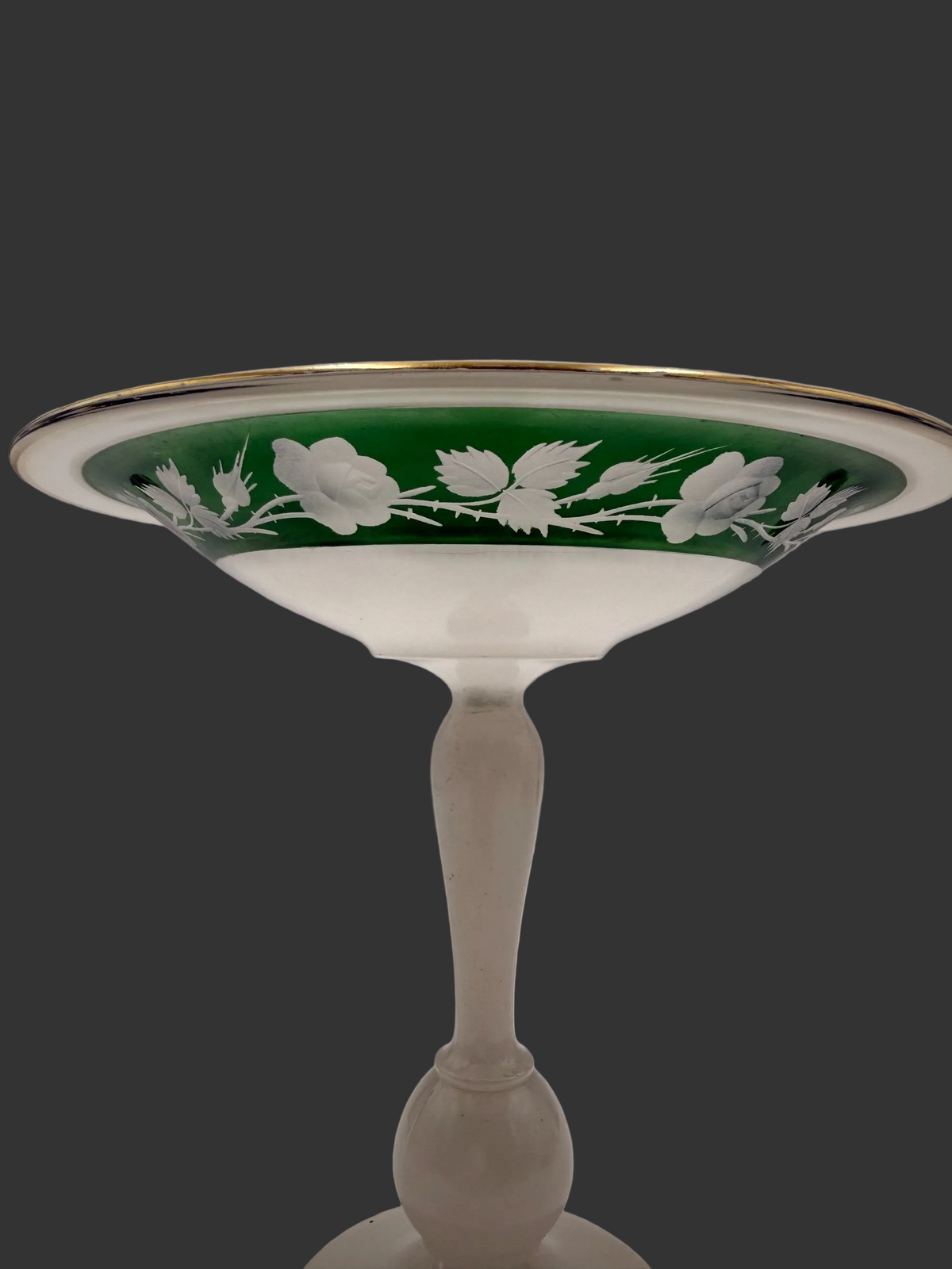 An antique-style glass pedestal bowl with a white body, a green band decorated with white floral motifs, and a thin gold rim, set against a neutral gray background.