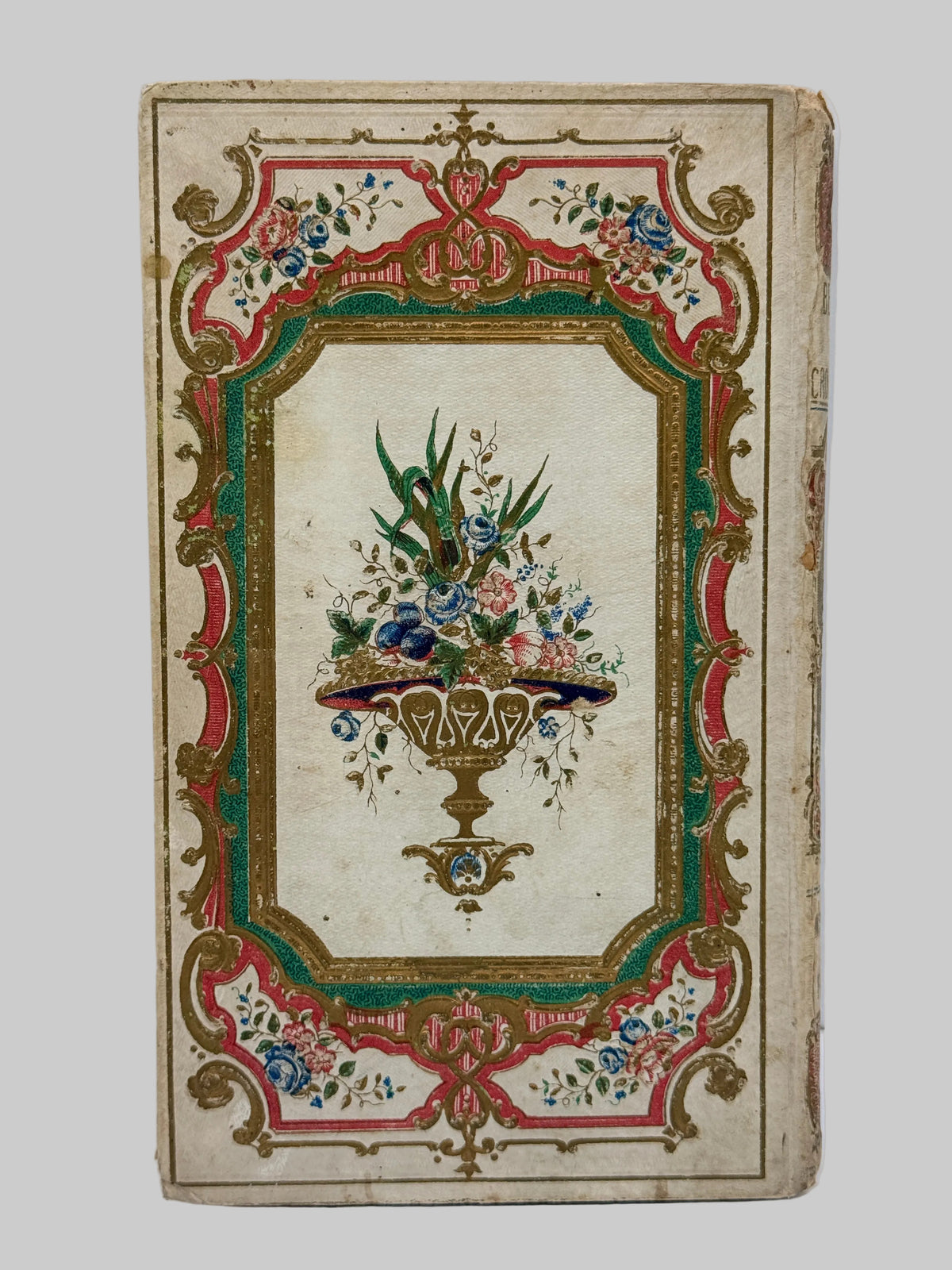 An antique decorative book or album cover with an ornate floral and scroll border in red, green, gold, and blue on a cream background, featuring a central painted bouquet in a vase.