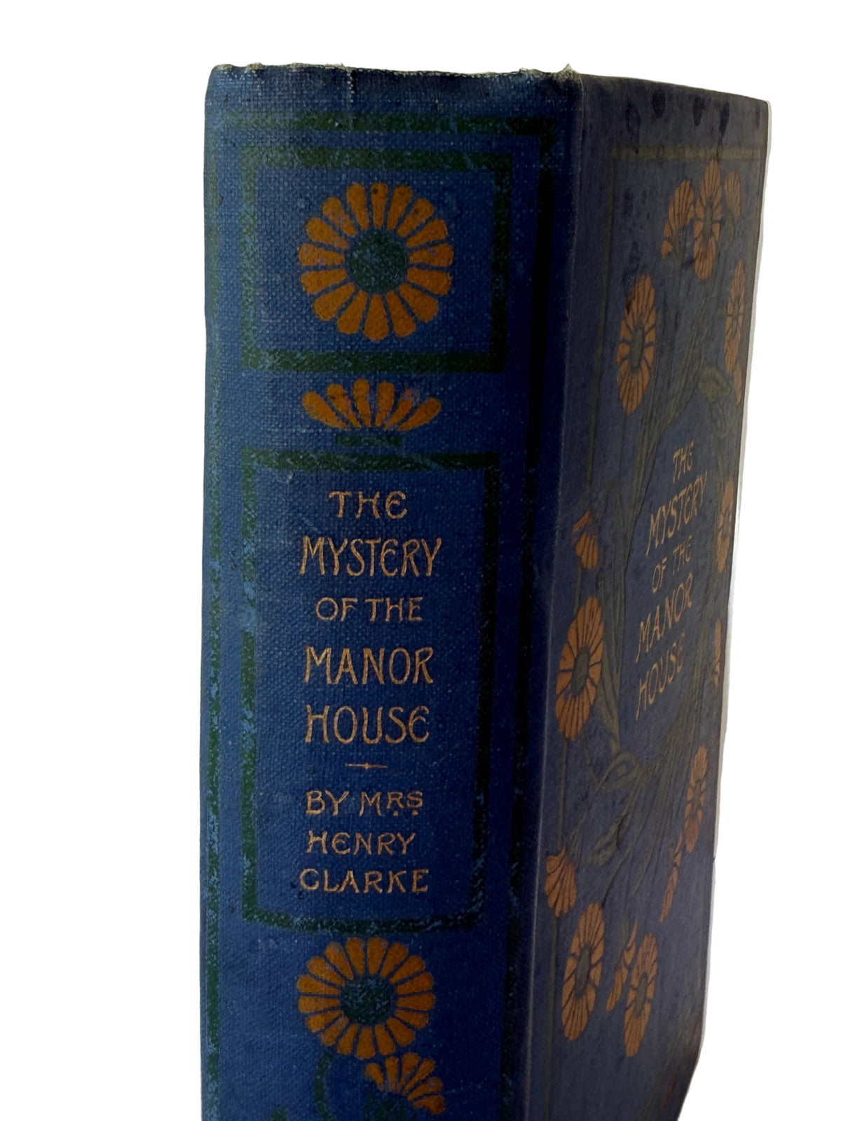 A vintage hardcover book titled 'The Mystery of the Manor House' by Mrs. Henry Clarke, featuring a dark blue cloth binding with gold floral and geometric border designs.