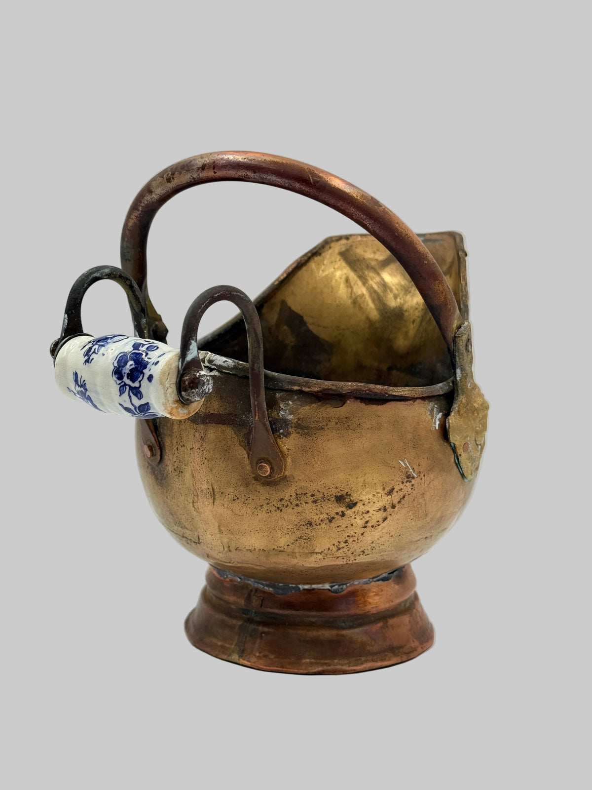 An antique copper pitcher with a decorative blue and white ceramic tag hanging from its handle, set against a plain white background.