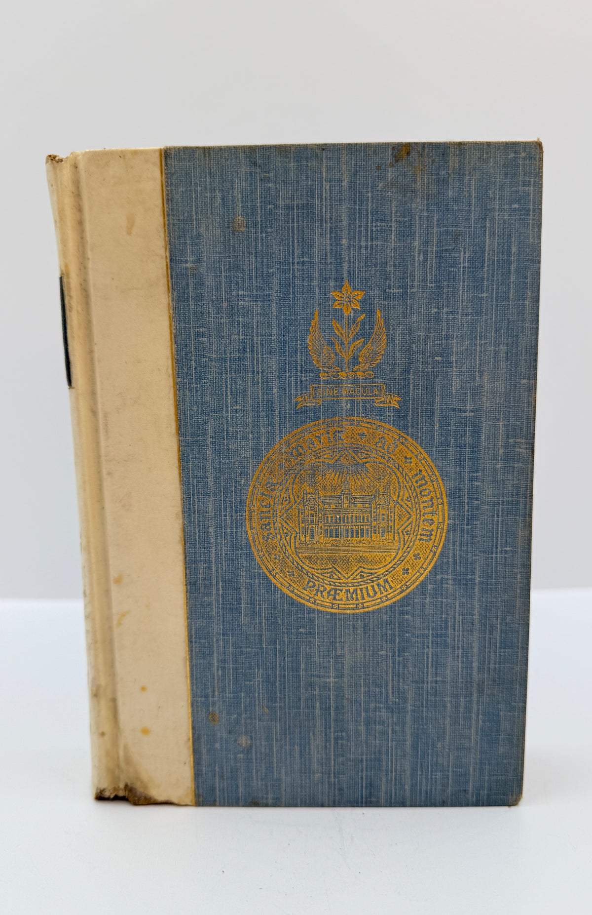 An antique hardcover book with a textured blue cloth cover and a gold embossed seal on the front, standing upright against a plain white background.