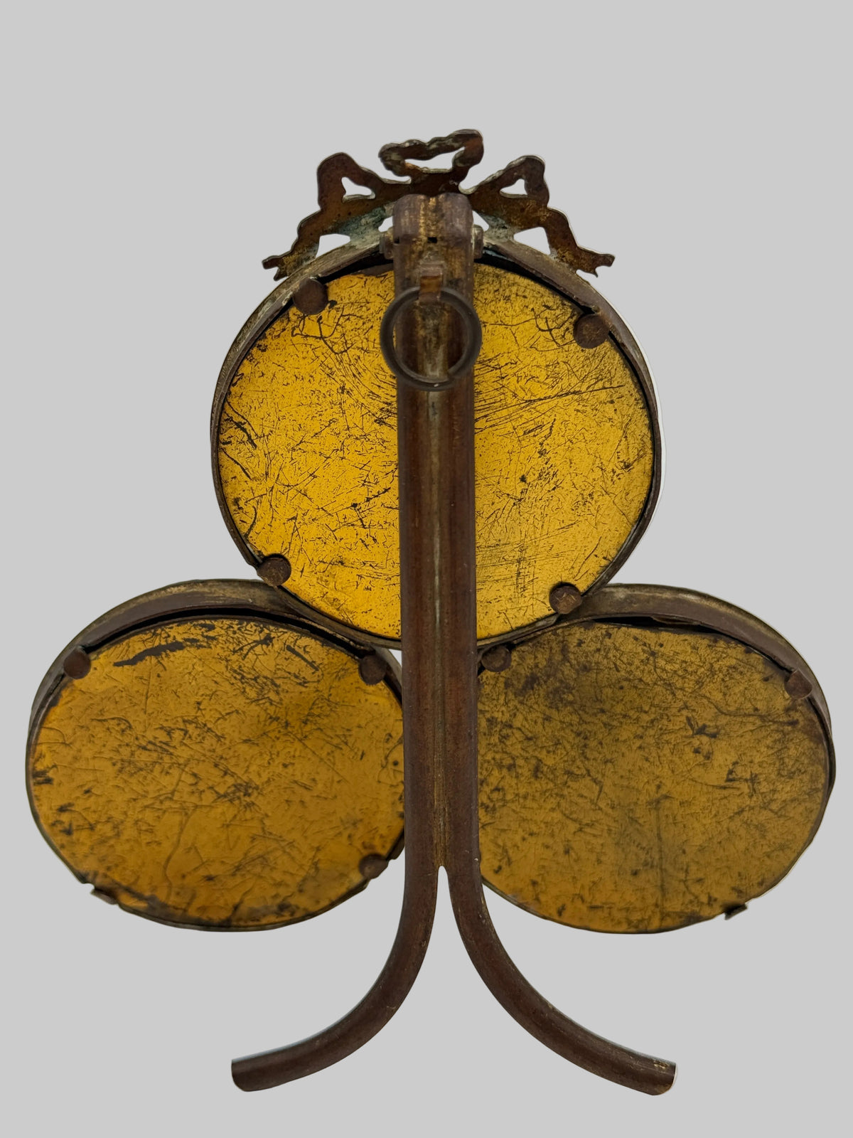 A vintage three-drum set with round gold-toned metal heads and dark brown wooden stands, photographed against a neutral light gray background.