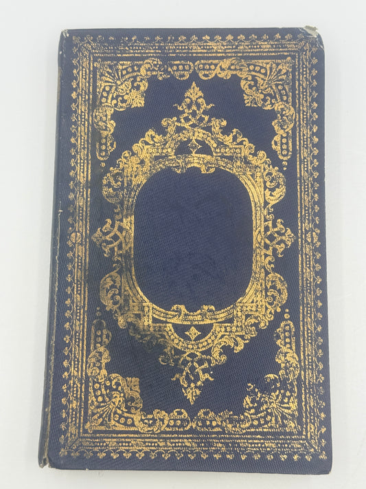 A vintage hardcover notebook or book with a dark navy blue cloth cover and ornate gold foil detailing, featuring a central oval cutout.