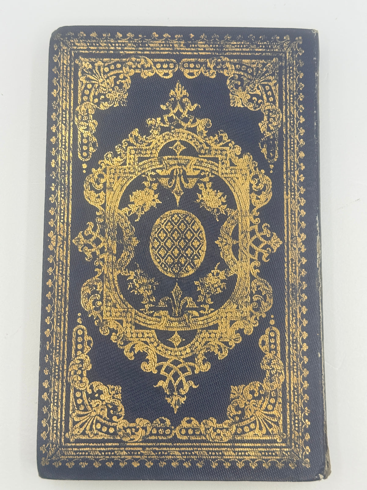 An antique hardcover notebook or journal with an ornate gold foil design on a dark navy blue cover, photographed flat against a white background.