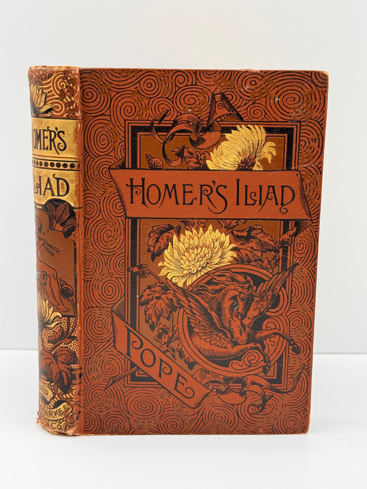 An antique book titled 'Homer's Island' by Pope, featuring a detailed brown and gold illustrated cover with a dragon and floral motifs, photographed against a plain white background.