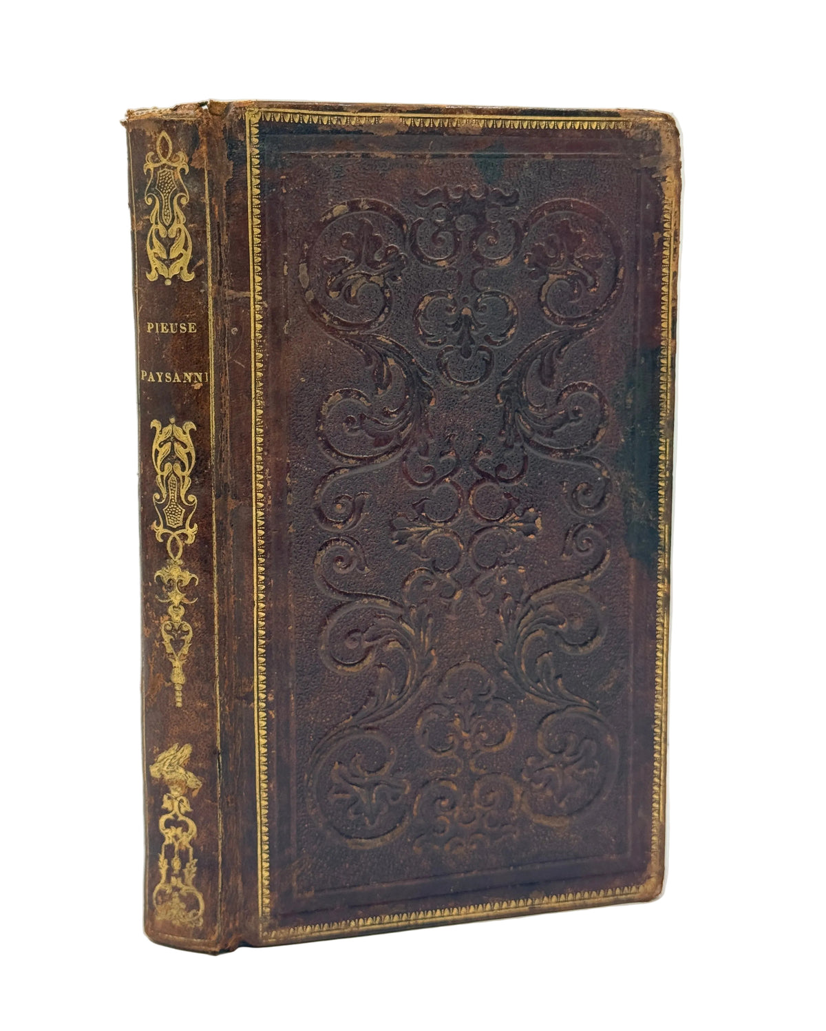 An antique leather-bound book with embossed floral patterns on the front cover and gold detailing on the spine, photographed against a plain light background.
