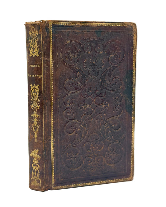 An antique leather-bound book with embossed floral patterns on the front cover and gold detailing on the spine, photographed against a plain light background.