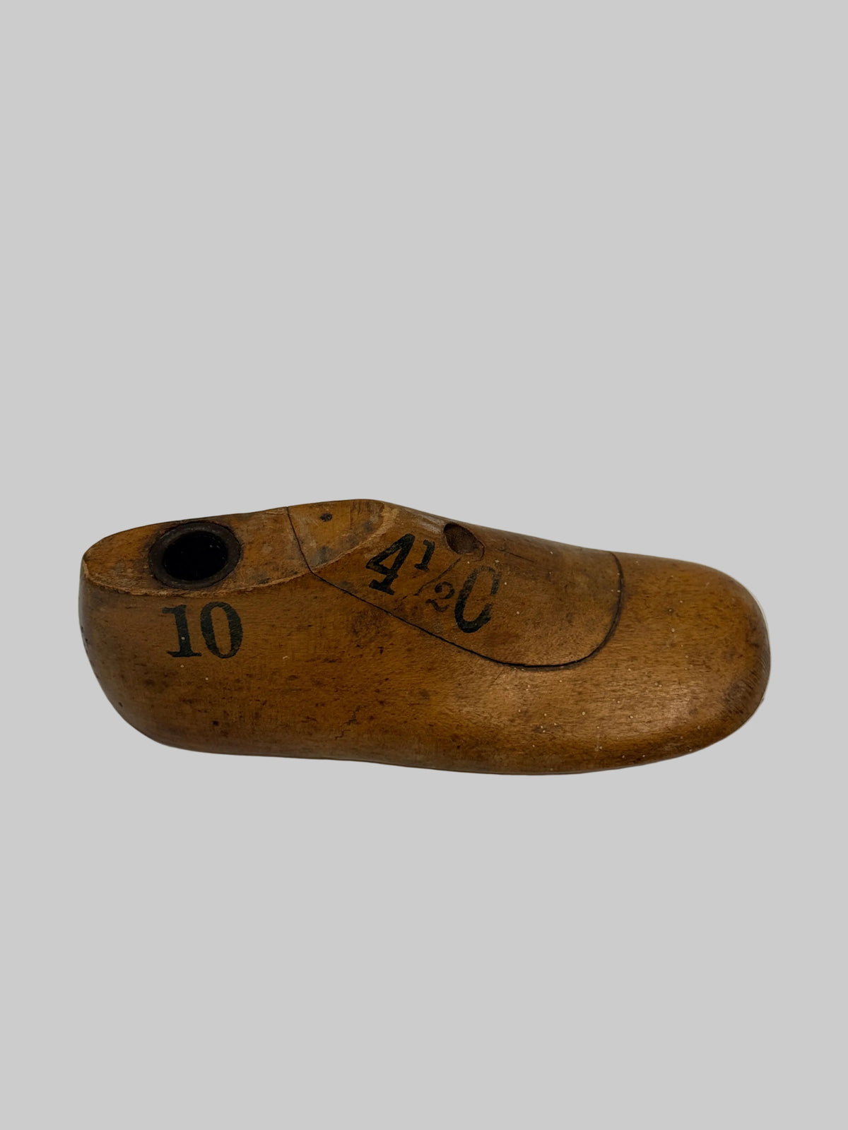 A small carved wooden shoe-shaped object with a circular hole near one end and black printed numbers and markings, photographed on a plain light background.