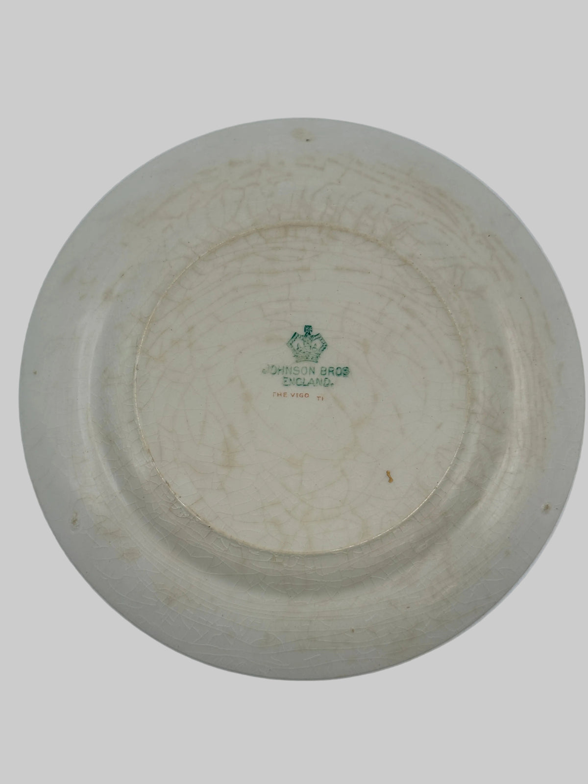 An off-white ceramic plate shown from the bottom side, featuring a green printed 'LONDON BRIDGE ENGLAND' crest and text in the center, set against a plain light background.