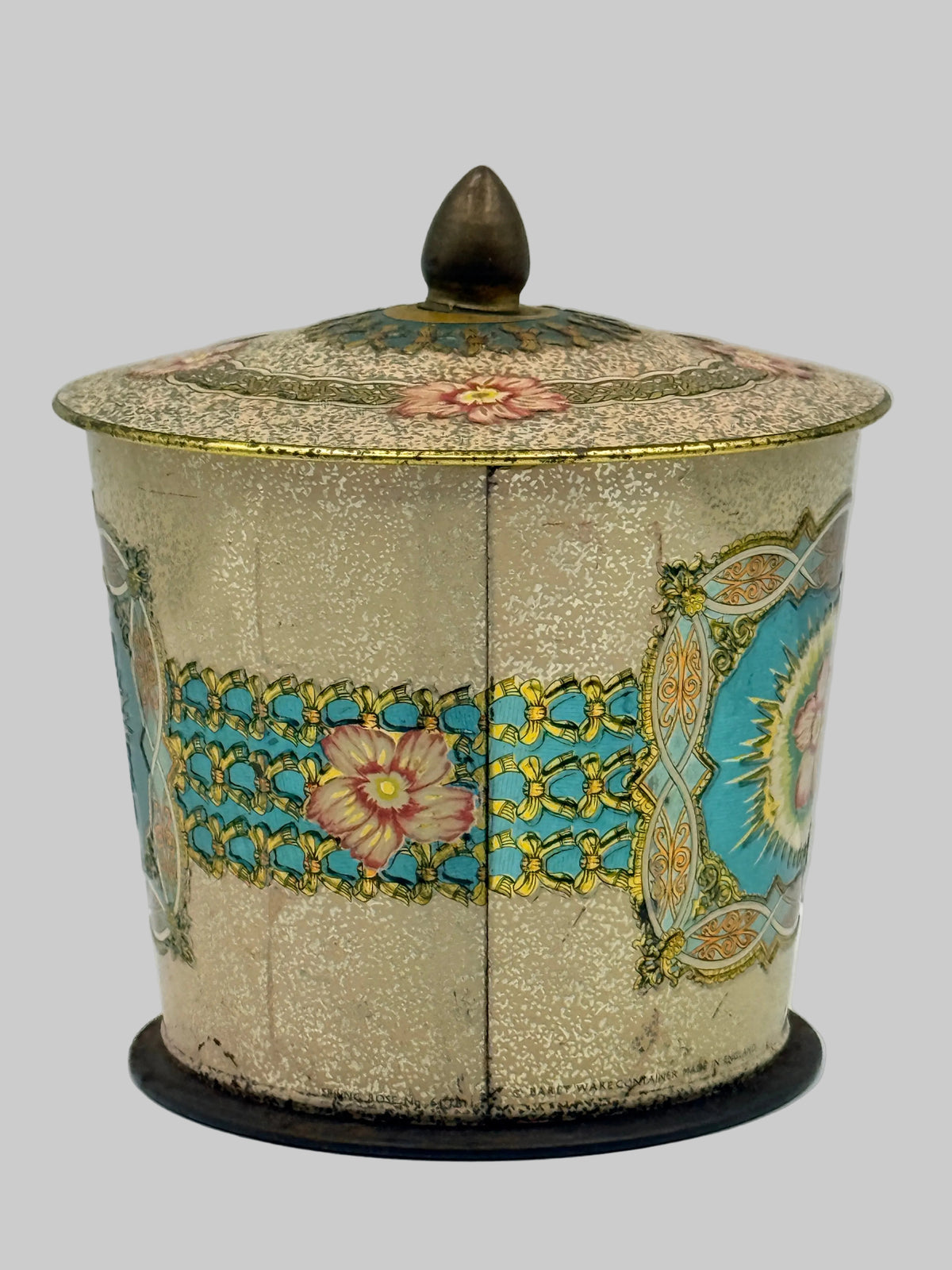 An antique decorative lidded box with a textured gold-beige body, turquoise and gold floral patterns, and a dark brown wooden finial on top, set against a plain light gray background.