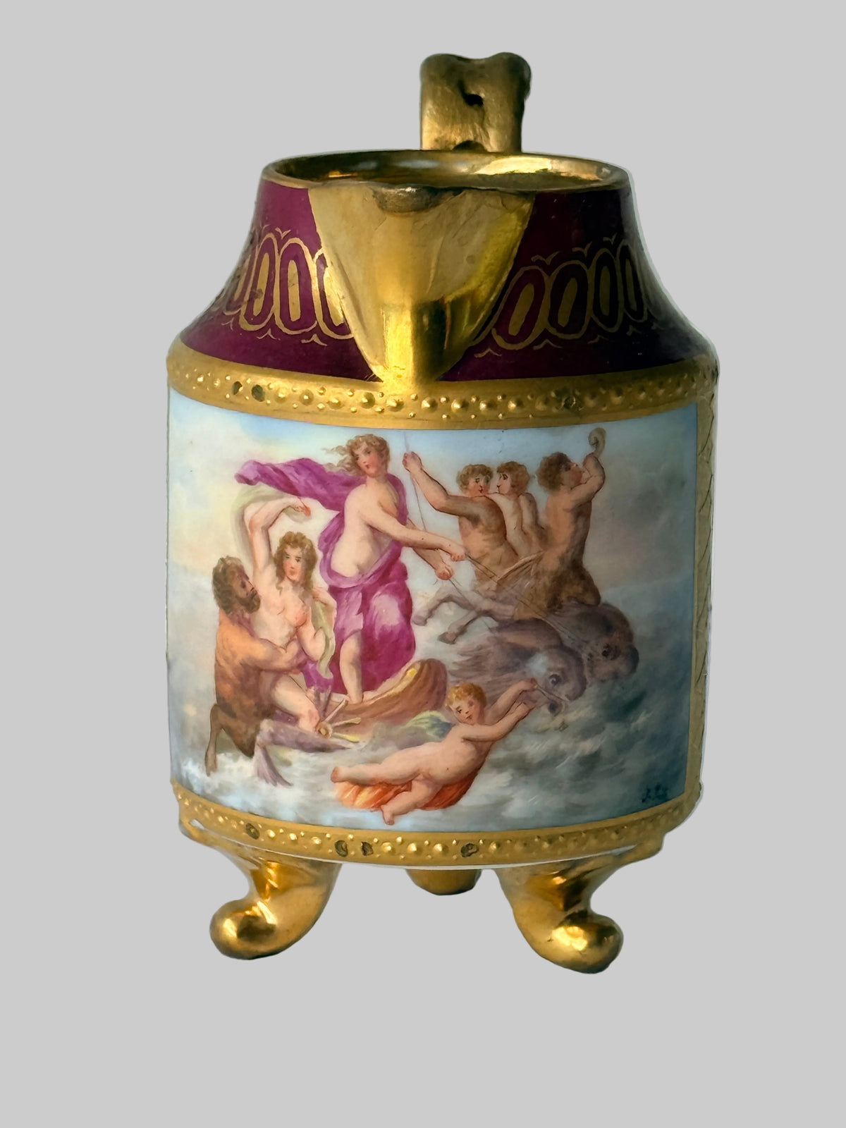 An ornate porcelain teapot with a gold-tone body, gold feet, and a purple and gold decorated neck. The front features a hand-painted classical scene with figures and horses on a light blue background.