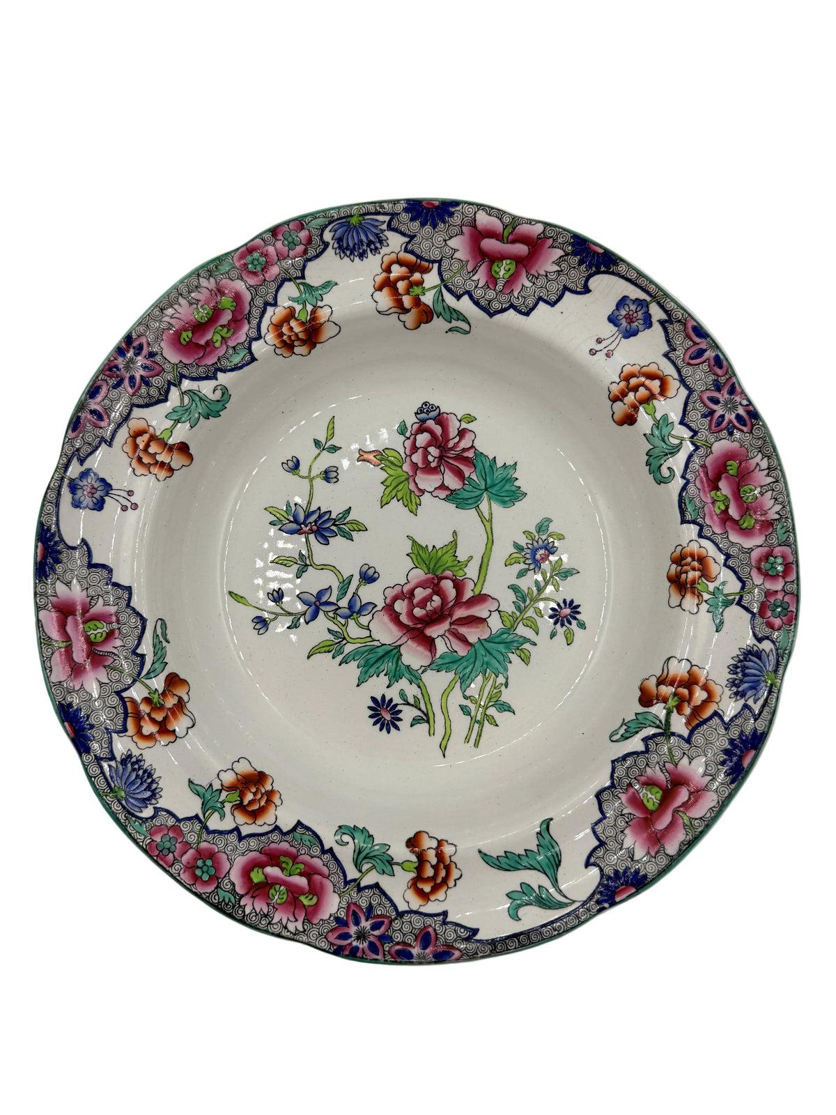A round ceramic plate with a white base, decorated with a colorful floral pattern featuring pink roses, green leaves, and blue and orange blossoms, set against a plain light gray background.