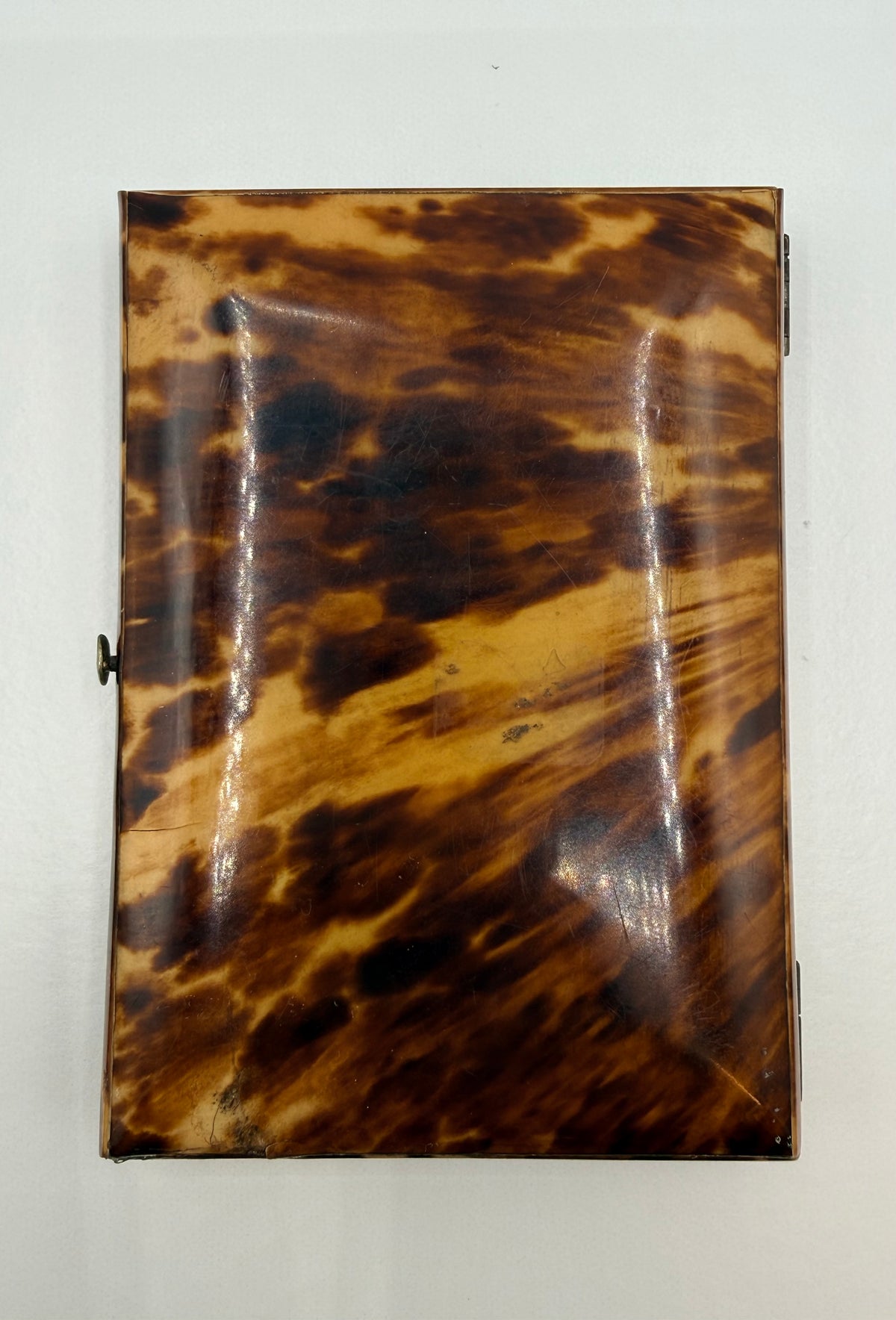A rectangular tortoiseshell case with a glossy finish, featuring a mottled pattern of dark brown, amber, and black, photographed against a plain off-white background.