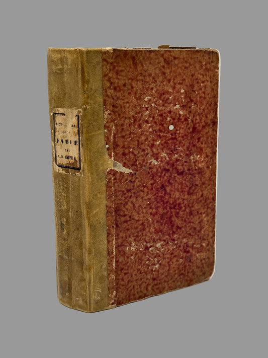 An antique hardcover book with a textured reddish-brown front cover and a tan spine, standing upright on a white surface against a light gray background.