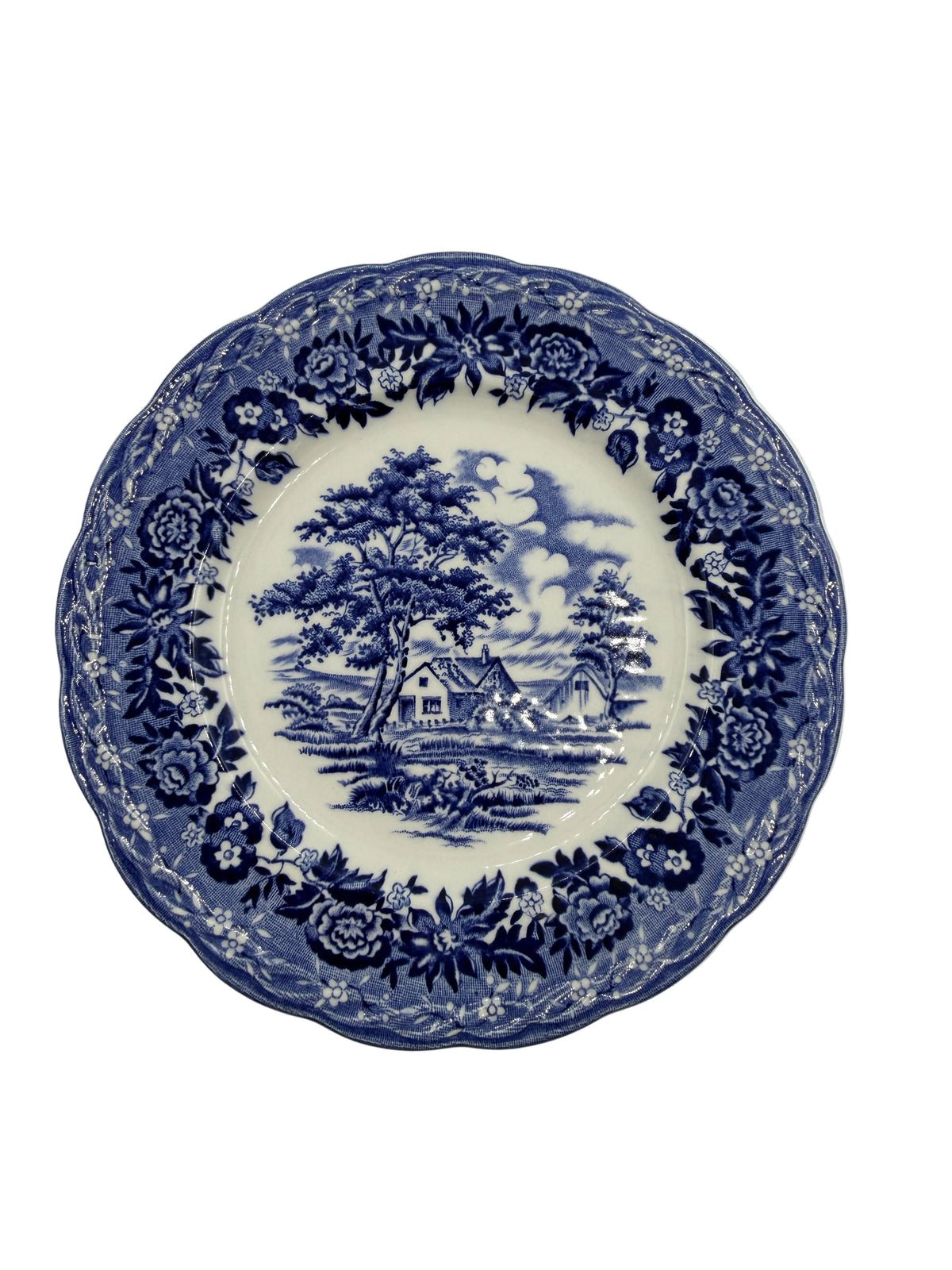 A round ceramic plate with a blue and white transfer print featuring a scenic landscape in the center and a floral border, shown against a plain light background.