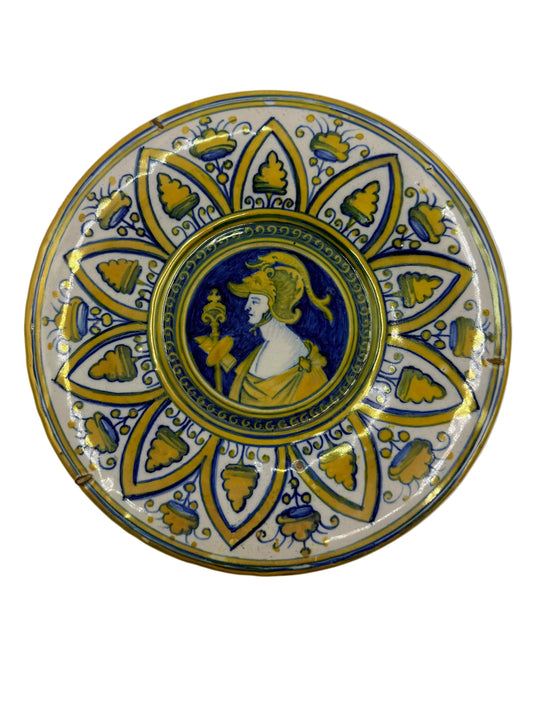 A round decorative ceramic plate featuring a central classical bust in blue and gold, surrounded by a blue and gold floral mandala pattern on a white background.