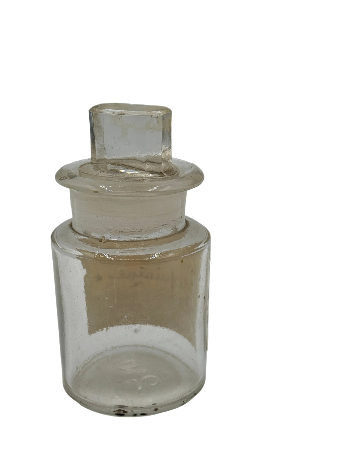 A small empty clear glass bottle with a matching glass stopper, photographed against a plain light gray background.