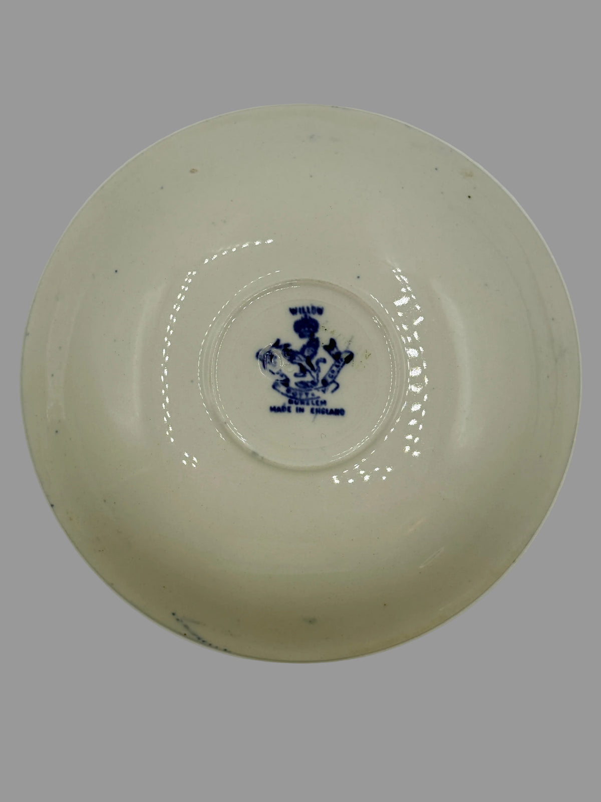 An off-white ceramic bowl viewed from above, featuring a small blue printed crest or emblem in the center.