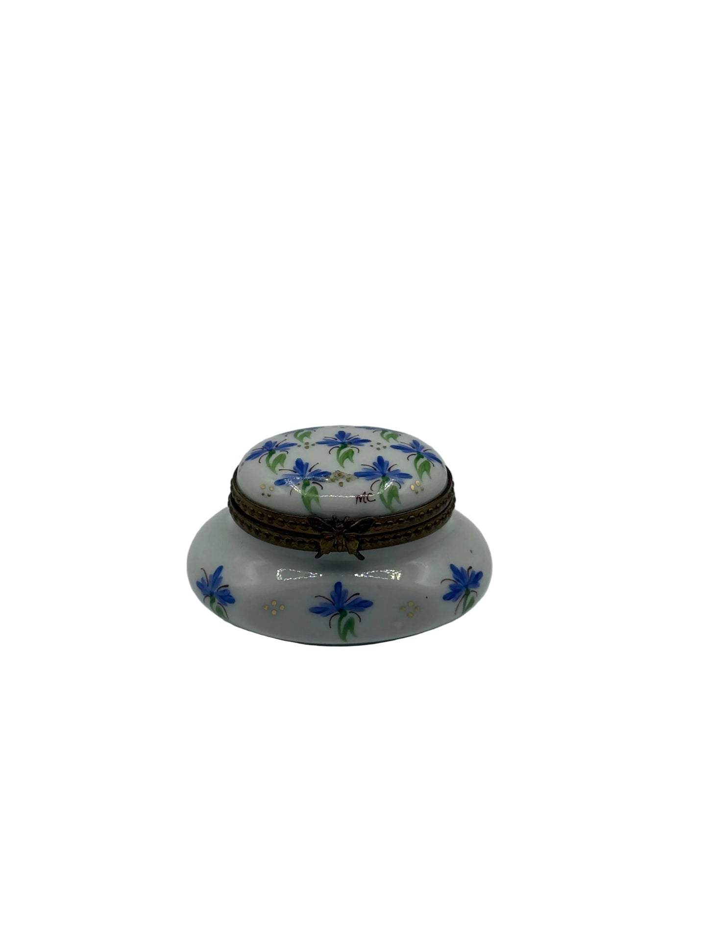 A small white ceramic lidded box decorated with blue flowers and green leaves, featuring a brown braided cord closure, set against a plain light gray background.