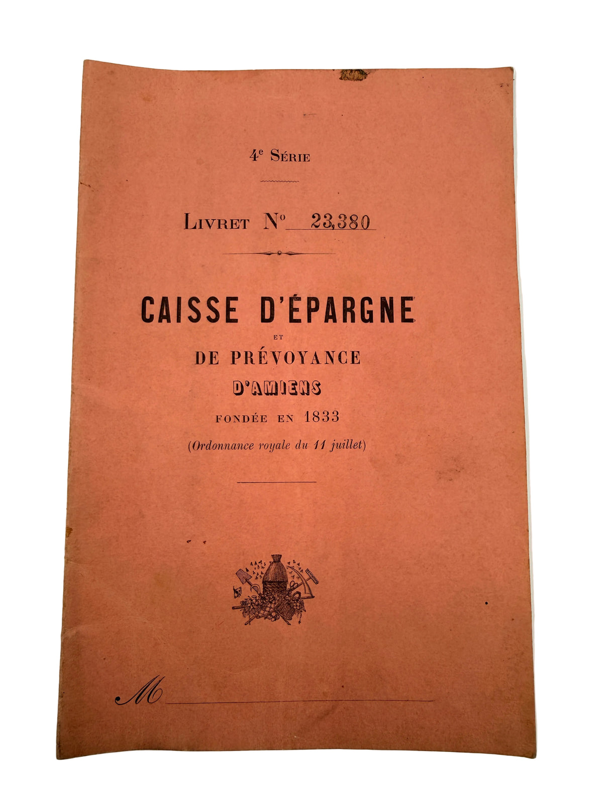 A vintage French savings notebook cover titled 'CAISSE D'EPARGNE ET DE PRÉVOANCE D'AMIENS' in black print on an orange-brown paper background, photographed flat against a light neutral surface.