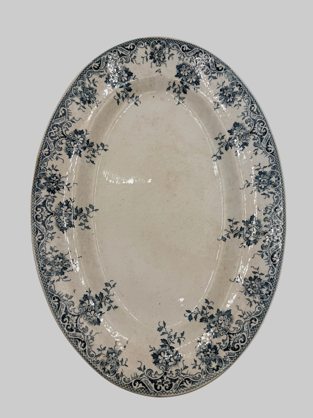 An oval ceramic serving platter with a cream-colored glaze and a dark blue floral and scroll border pattern, shown against a plain light background.