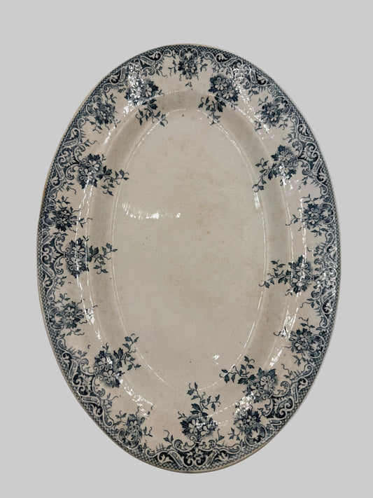 An oval ceramic serving platter with a cream-colored glaze and a dark blue floral and scroll border pattern, shown against a plain light background.