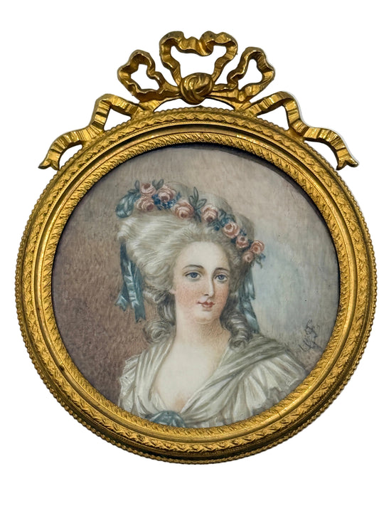 An oval framed portrait painting of a woman with a floral hairpiece, set in an ornate gold frame with a decorative top crest, shown against a plain light background.