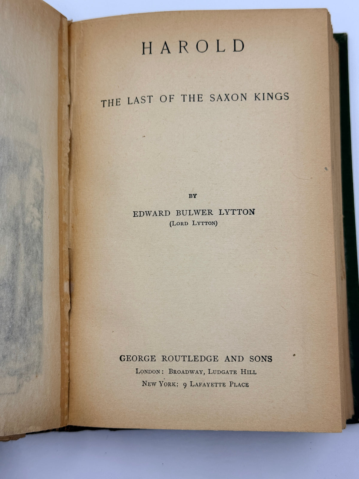 An open vintage book showing the title page for 'Harold: The Last of the Saxon Kings' by Edward Bulwer Lytton, published by George Routledge and Sons. The pages are a warm, aged tan paper with black printed text, and the book is photographed against a light gray background.