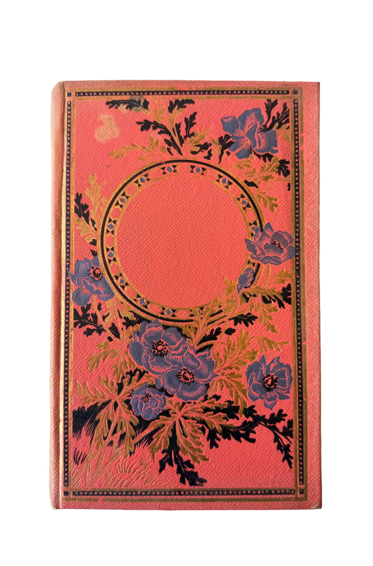 A vintage hardcover book or notebook with a textured coral-pink cover, decorated with blue flowers and gold-toned botanical details surrounding a central blank oval.