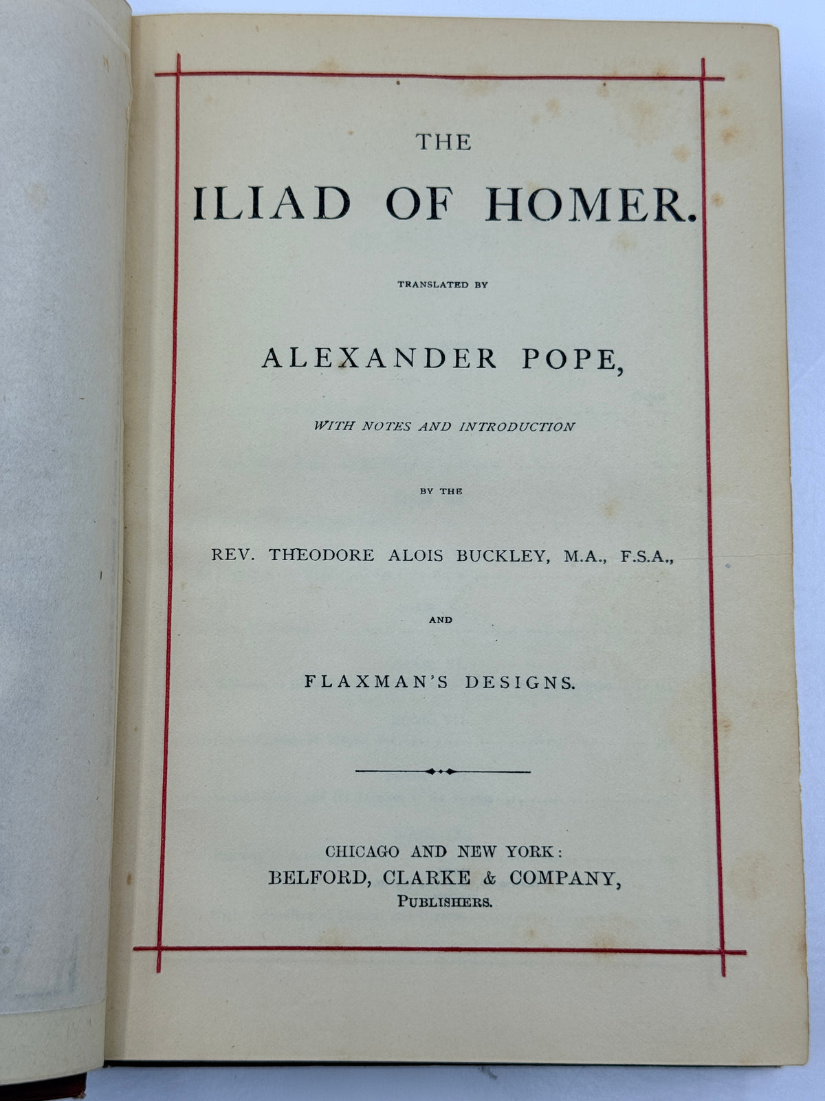 Open vintage book showing the title page of 'The Iliad of Homer' translated by Alexander Pope, with black serif text, a red border line, and aged cream paper on a light background.