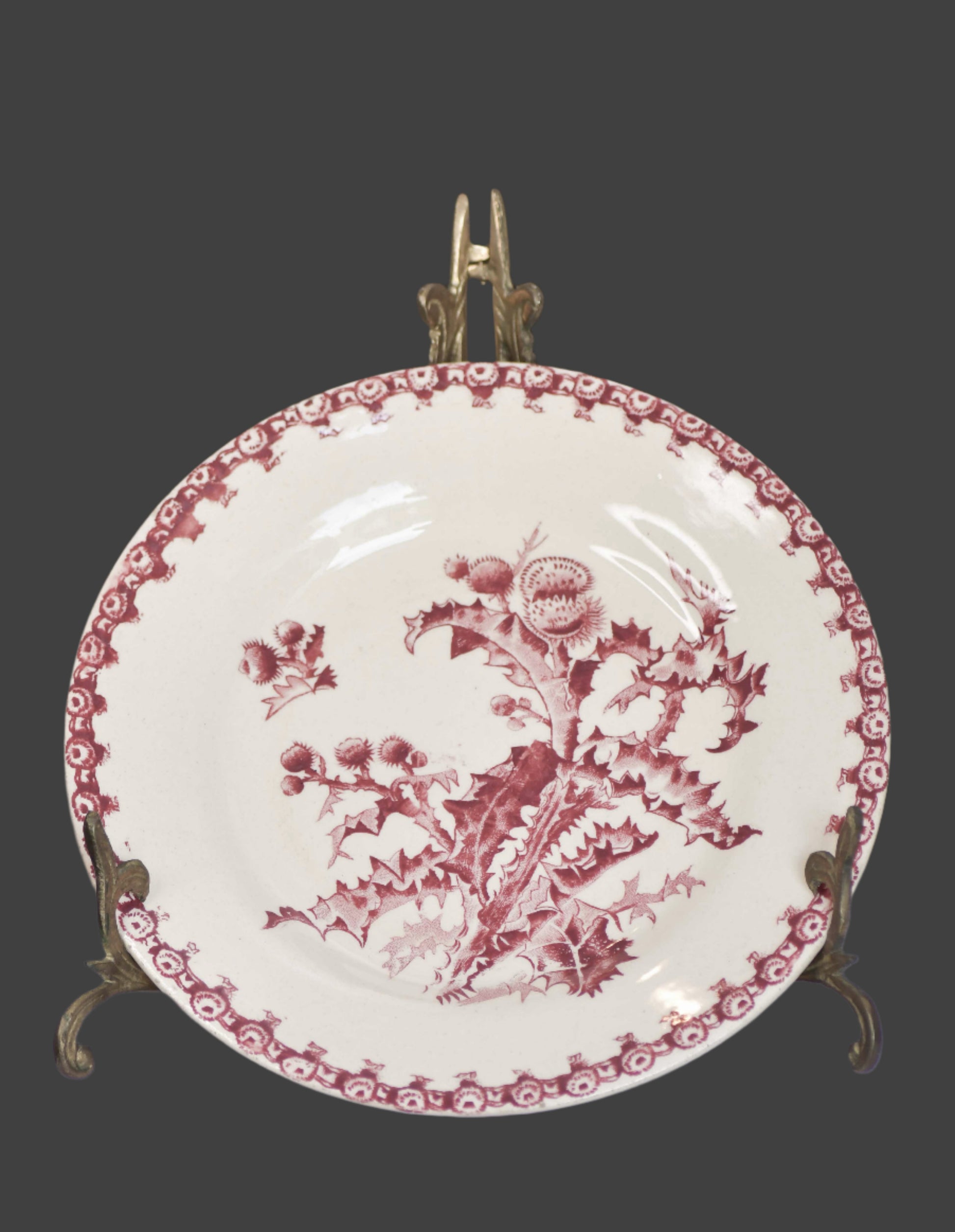 An antique French porcelain or ironstone plate with red transferware decoration featuring botanical leaves and floral sprouts on a white background, displayed on a stand.