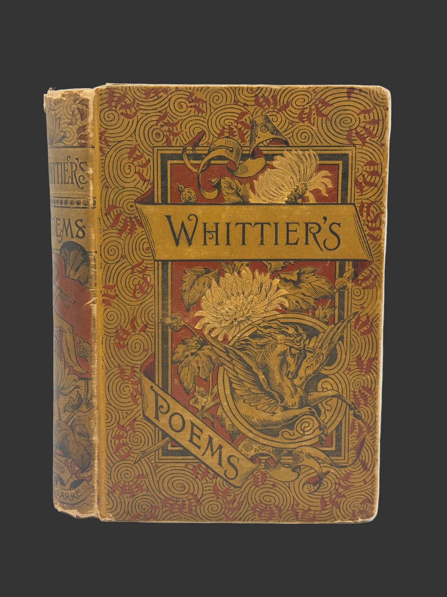 An antique hardcover book titled 'Whittier's Poems' with ornate gold and red floral patterns on a brown cover, photographed against a plain light background.