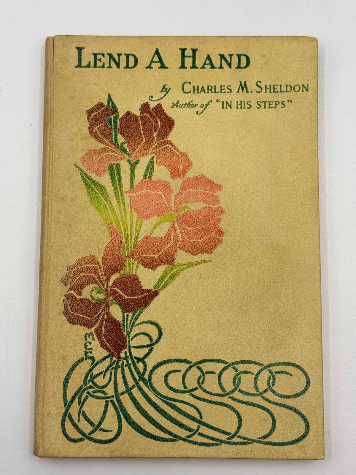 Antique hardcover book titled 'Lend A Hand' by Charles M. Sheldon, featuring an illustrated floral design on a tan cover with green and orange-brown accents.