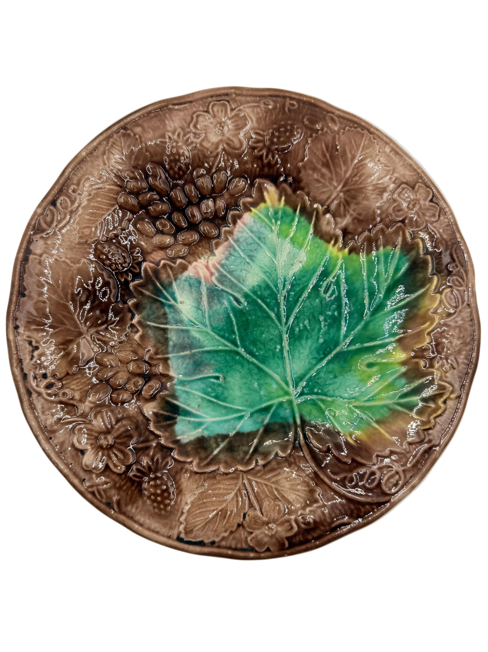 An oval ceramic plate with embossed grapevine and leaf patterns in a glossy brown glaze, featuring a large green grape leaf design in the center, shown on a light gray background.