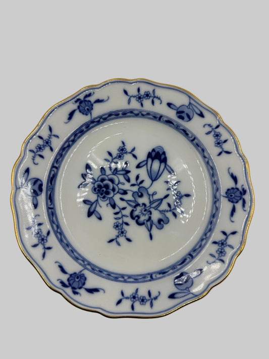 A scalloped ceramic plate with a blue floral pattern and gold trim, photographed from directly above on a plain white background.