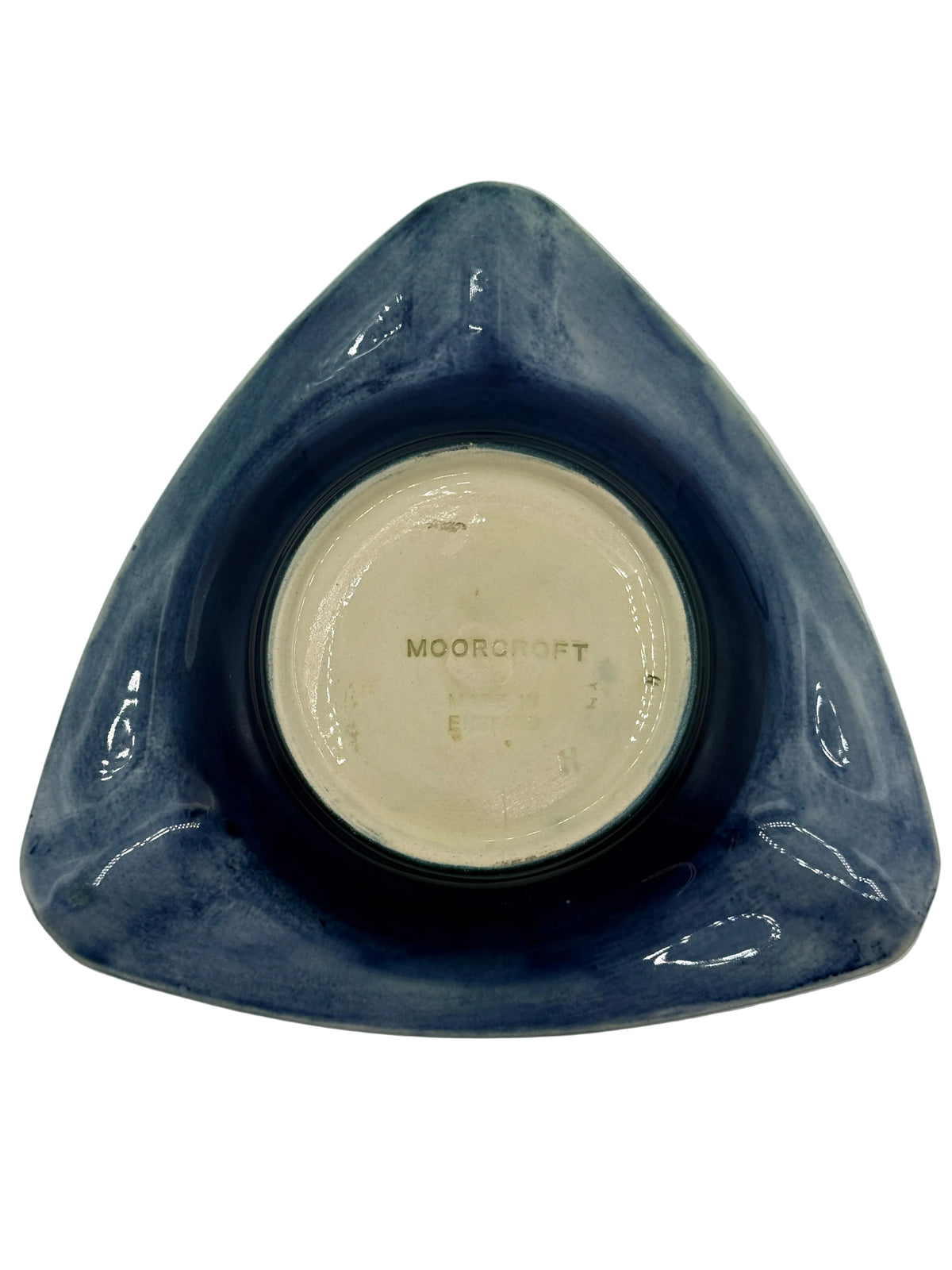 A vintage Moorcroft triangular ceramic dish with a glossy dark blue glazed exterior and a cream-colored unglazed center, photographed from directly above on a white background.