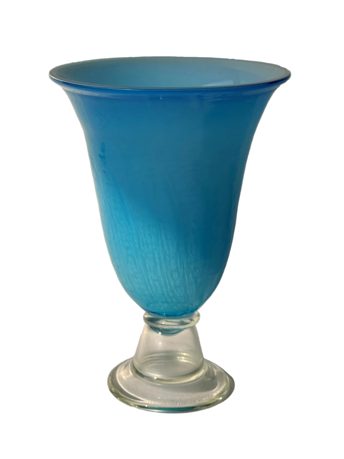 A vintage cobalt blue glass vase with a flared rim and a clear glass pedestal base, set against a white paneled wall with soft sunlight and shadows.