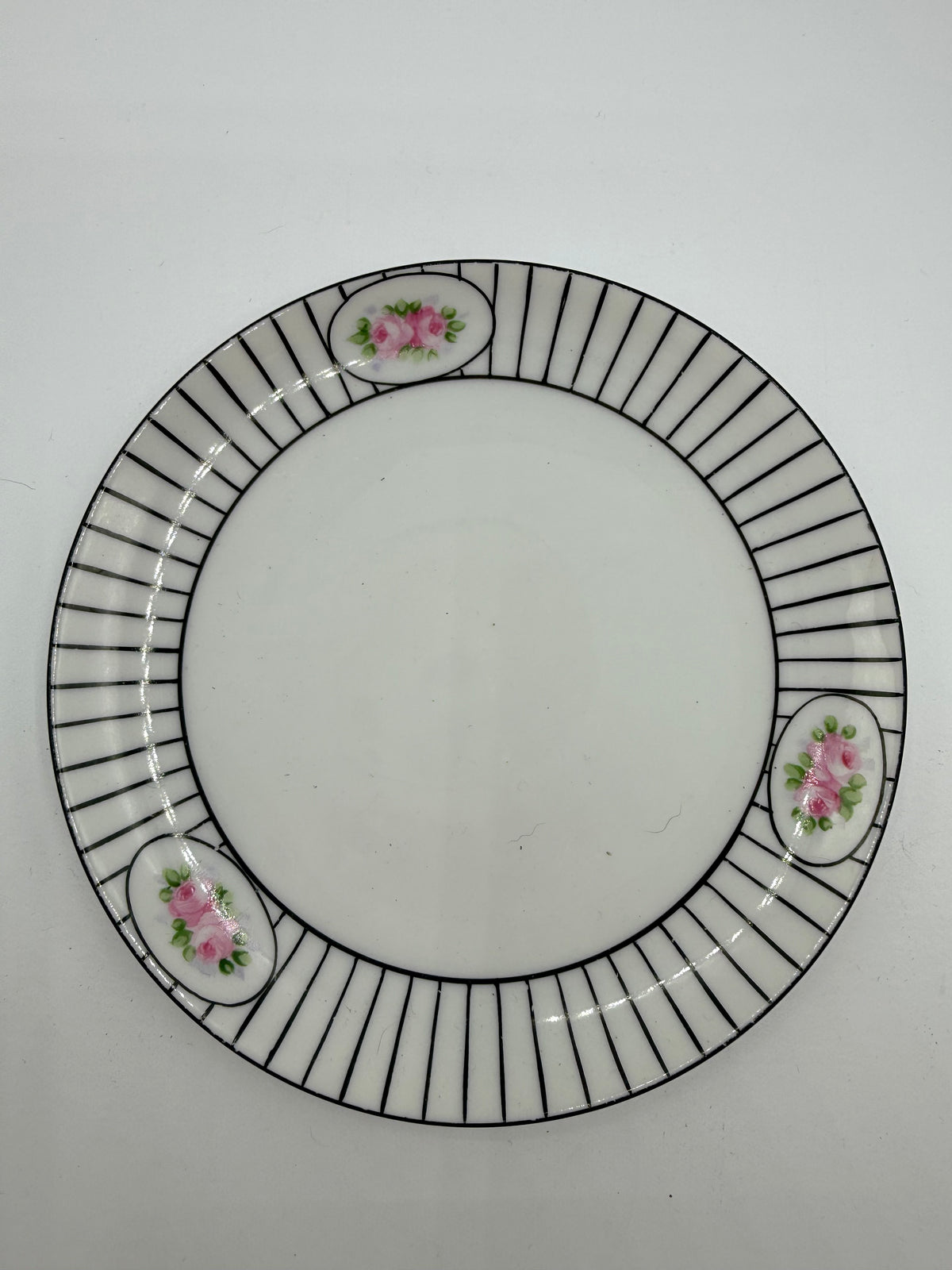 A white ceramic plate with a black radial striped border and three small pink floral accents, photographed from above on a light gray background.