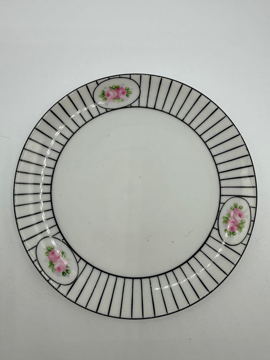 A white ceramic plate with a black radial striped border and three small pink floral accents, photographed from above on a light gray background.